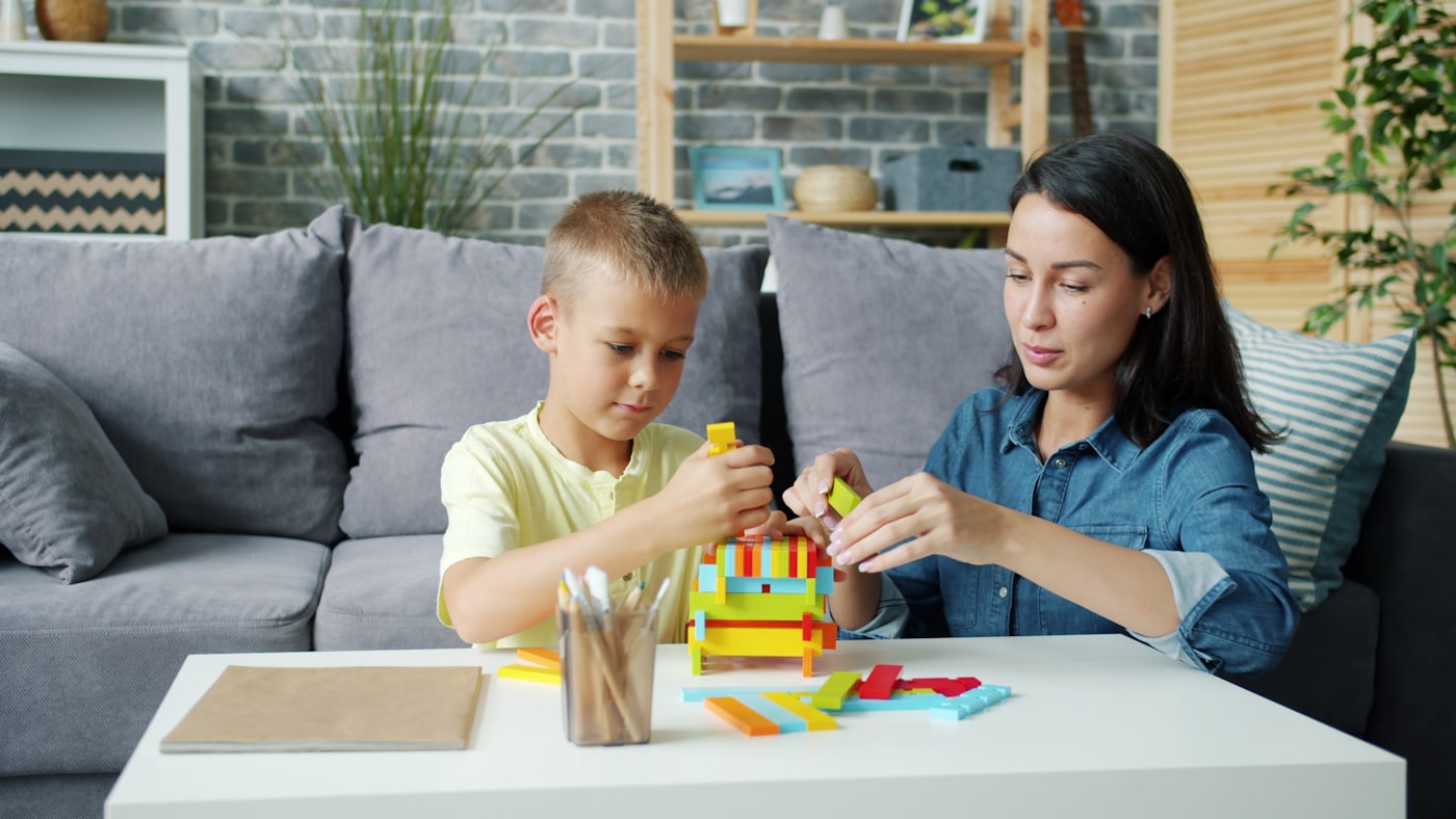 A caring therapist and a young child building with colorful blocks together